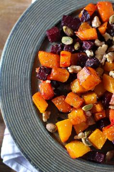 a plate full of roasted vegetables and nuts on top of a wooden table with napkins