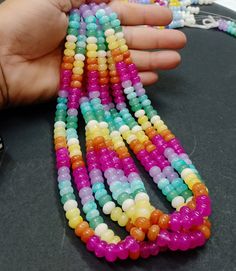 a hand holding several multicolored beads on top of a black table next to a cell phone