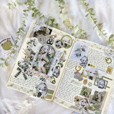 an open book with various pictures on it and some green leaves around the pages, sitting on top of a white sheet