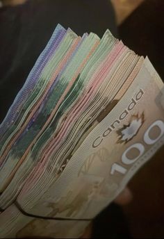 a person is holding up a stack of canadian currency in their hand, with the number 100 on it