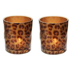 two leopard print cups sitting next to each other on a white surface with one candle in the middle