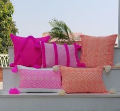 pink and orange pillows sitting on top of a white bench next to a palm tree