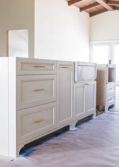 an unfinished kitchen with white cabinets and blue tape on the floor in preparation for painting