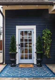 two potted plants are on the front porch of a blue house with white trim