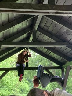 three people hanging out on the roof of a building with trees in the back ground