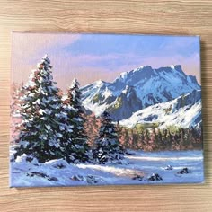 a painting of snow covered pine trees in front of mountains on a wooden table top