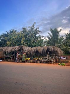 a woman standing in front of a hut with thatched roof and tables under it