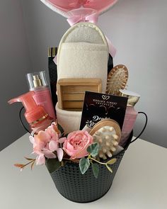 a basket filled with lots of different items on top of a white table next to a pink heart shaped balloon