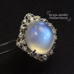 This large rare Moonstone Cabochon Ring is set in 14k solid gold and exhibits mesmerizing blue flash aduralescence. Scintillating diamonds surround this natural beauty! Ring Size: 5.75 Total Weight: 13.65 grams Precious Metal: 14k solid gold Precious stones: -Moonstone Center Stone: 18.5mm x 16.2mm, 23.05 carats -White Round Diamond: 0.4ct Elegant Moonstone Ring With Gemstone Accents, Elegant Multi-stone Moonstone Ring, Fine Jewelry White Gold Moonstone Cabochon Ring, Celestial Round Moonstone Ring For Formal Occasions, Formal Moonstone Ring With Gemstone Accents, Celestial Moonstone Ring With Gemstone Accents, Celestial Moonstone Ring For Formal Occasions, Moonstone Ring With Diamond And Gemstone Accents, Unique Moonstone Ring With Accent Stones