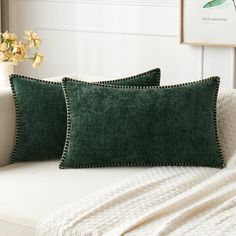 two green pillows sitting on top of a white couch next to a vase with flowers