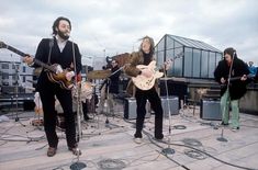 a group of people standing on top of a roof playing guitars and singing into microphones