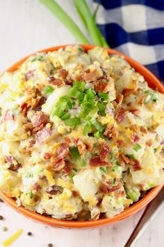 an orange bowl filled with potato salad on top of a white wooden table next to green onions