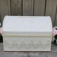 a white box with lace on it sitting next to some flowers and wood planks