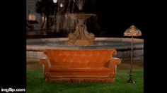 an orange couch sitting in front of a fountain at night with a lamp on it