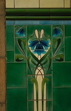 a green tiled wall with blue flowers and leaves painted on it's glass panels