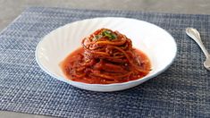 a white bowl filled with spaghetti on top of a blue place mat next to a fork