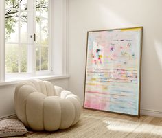 a large painting sitting on top of a wooden floor next to a white chair in front of a window