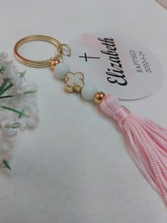 a pink tasseled keychain sitting on top of a white table next to flowers