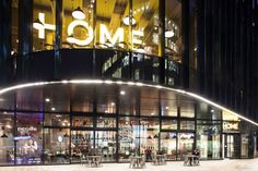 an illuminated building with people sitting at tables in front of it and the word home on top