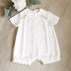 This Little Baby Boy's Romper Is A Classic! The Outfit Is Done Is A Soft Cotten Blend Twill In A Soft White Hue. The Peter Pan Point Collar Adds A Dressier Element To The Romper. The Shoulders Have Sweet Beige Buttons, Three On Each Side Just Below A Matching Beige Piping Trim. Relaxed Fit In The Legs. Elastic Leg Opening In The Back For Comfort And A Matching Band In Front For A Tailored Style. A Three-Button Inseam Make For Easy Changes. The Back Has Darts At The Shoulders That Fall Into Soft Cotton Bubble Romper With Short Sleeves For Baptism, Cream Short Sleeve Bubble Romper For Summer, White Fitted Bubble Romper For Playwear, Fitted White Bubble Romper For Play, White Short Sleeve Bubble Romper For Baptism, Summer Baptism Dress With Short Sleeves, White Bubble Romper For Baptism In Summer, White Bubble Romper For Baptism, White Short Sleeve Bubble Romper For Playwear