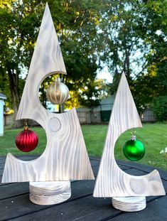 two metal christmas trees on top of a wooden table in front of some grass and trees