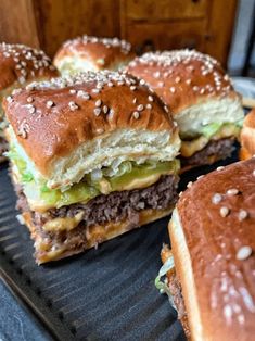 three hamburgers with cheese, lettuce and other toppings on a grill