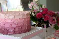 a pink and white cake sitting on top of a table next to some pretty flowers