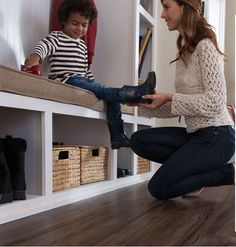 a woman kneeling down on the floor next to a little boy holding a pair of boots