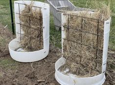 two white containers filled with hay sitting in the grass