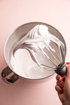 a hand holding a whisk over a metal bowl filled with white whipped cream