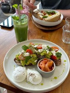 a white plate topped with lots of food on top of a wooden table next to a drink