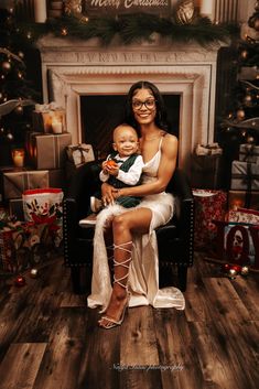 a woman sitting on a chair holding a baby in front of a christmas tree with presents