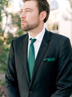 a man in a suit and green tie looking off to the side with his hand on his hip