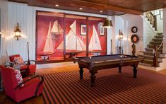 a pool table in a living room next to a stair case with sailboats on it