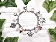 a silver bracelet with charms on it and leaves in the background, sitting on a white wooden surface