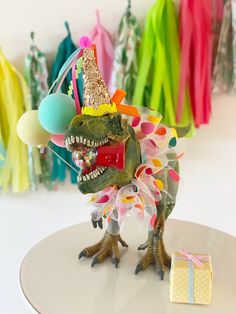 a toy dinosaur wearing a party hat with balloons and streamers on it's head