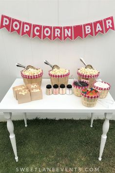 a table topped with lots of cupcakes next to a sign that says popcorn bar