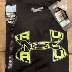 the under armour shirt is laying on the floor next to its tag and some other items