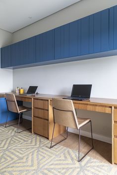 two laptops sitting on top of a wooden desk in front of a blue wall