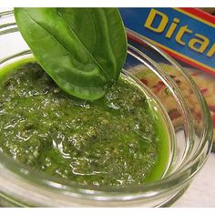 a glass jar filled with green sauce next to a box of pasta and spinach