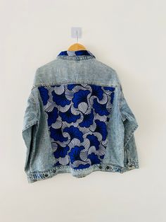 a denim jacket with blue and white designs hanging on a hanger in front of a white wall