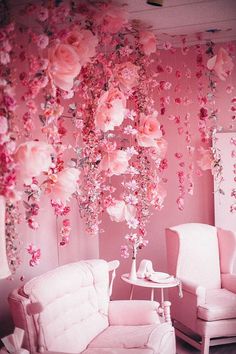 a living room with pink flowers hanging from the ceiling and two white chairs in front of it