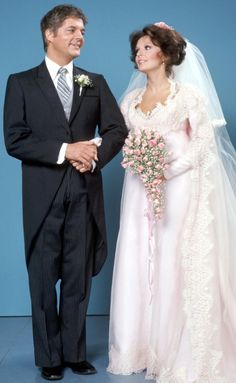 a man and woman standing next to each other in front of a blue wall holding hands