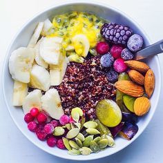 a bowl filled with fruit and nuts on top of a white countertop next to a spoon