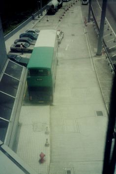 a green bus parked on the side of a road next to a parking lot filled with cars