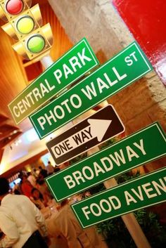 several street signs in front of a stoplight at an indoor mall with people walking around