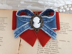 Denim and velvet bow brooch, Blue and rust orange brooch with cameo, Everyday accessory  Beautiful gift for girlfriend, women, wife, mother or daughter on Christmas or any other occasion. This handmade bow tie can be worn on a shirt, a dress, a sweater, a t-shirt or as an accessory for coat, bag or everything is allowed to be attached by a brooch or alligator clip 3.5 inch lengths 3 inch width Ready for shipping My Flower accessories are carefully packed in a sturdy box for shipping to make sure they arrive in the very best condition. Comes from non-smoker and pet free studio. Due to differences in computer monitors, actual colors may vary slightly from those shown I do take custom orders if you need more than one or desire a different color. It takes around a few days. Do not hesitate to Vintage Ribbon Brooches As Gift, Vintage Bow Tie Brooch As Gift, Vintage Ribbon Brooches, Vintage Bow Tie Brooch For Formal Occasions, Womens Bow Tie, Small Gifts For Women, Bow Tie Women, Tie Brooch, Denim Jewelry