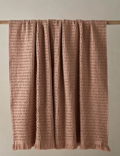 a pink blanket hanging on a clothes line with the curtain pulled back to reveal a crochet pattern