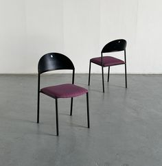 two black and purple chairs sitting next to each other on a cement floor in front of a white wall