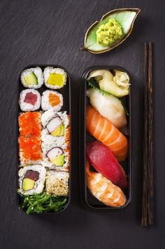 sushi and chopsticks on a black surface next to an empty container with two different types of sushi in it